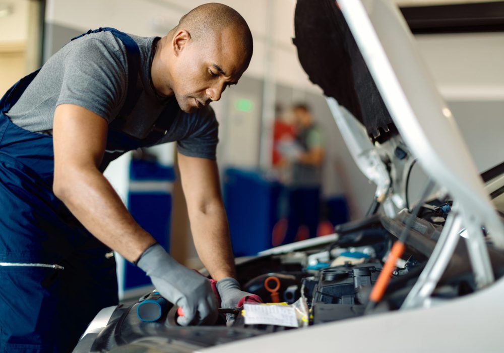 African American mechanic repairing car engine in a workshop. Black auto repairman using wrench while working on car engine in a workshop.