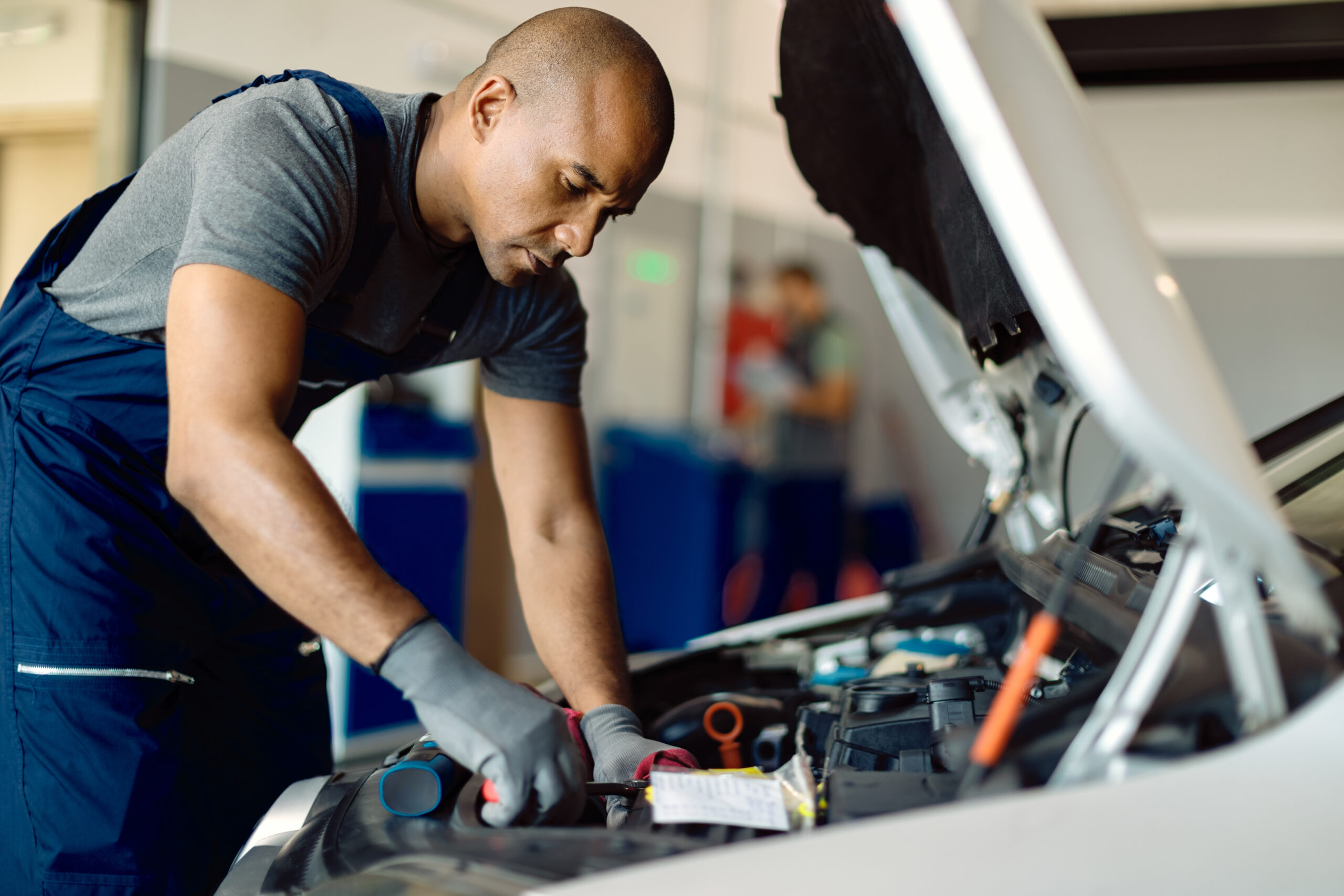 Black auto repairman using wrench while working on car engine in a workshop.
